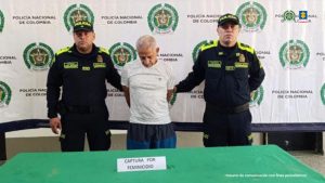 En la imagen aparece el capturado de pie y esposado, acompañado por dos uniformados de la Policía Nacional. Detrás de ellos un banner de la Policía Nacional