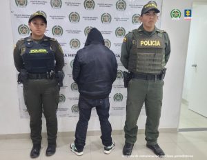 El detenido aparece de espaldas capturado junto a dos uniformados de la Policía Nacional. De fondo se ve un banner de la Policía