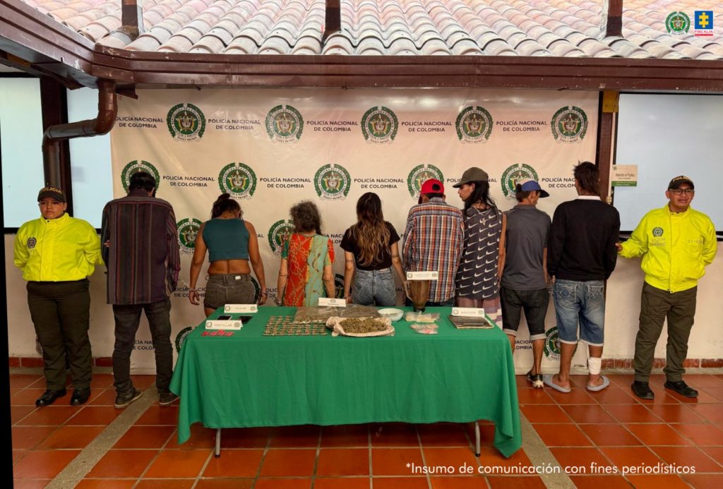 en la fotografia se puede ver a los 8 capturados entre dos agentes de po,icia, frente a ellos hay una mesa con todo el material incautado. Detras de ellos un baking de la policia nacional