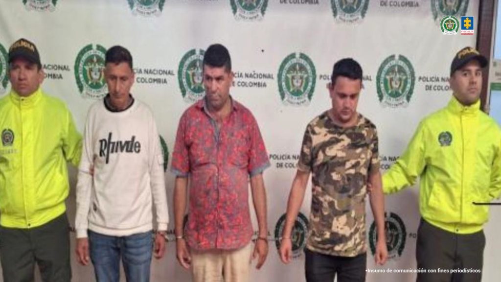 En la fotografia se ve a los 3 detenidos entre dos policias que los custodian, detras de ellos un baking de la policia