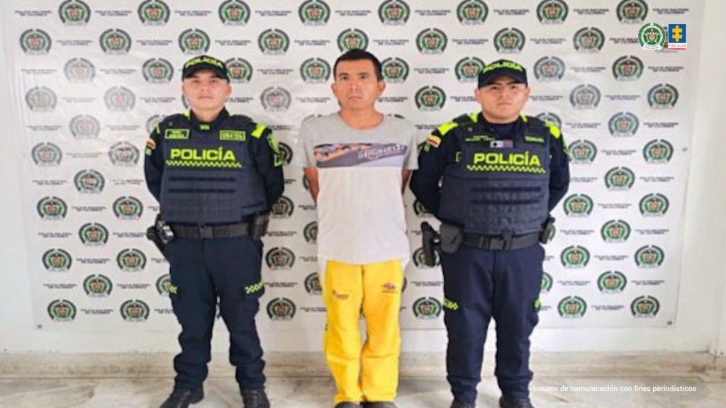 En la fotografía se observan tres personas una de ellas el capturado acompañado de dos uniformados de la Policía Nacional. 