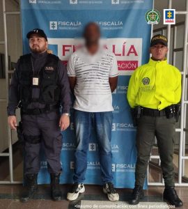 En la fotografía se encuentra el procesado con un pendón de la Fiscalía al fondo y un funcionario del CTI y otro de La Policía Nacional, uno a cada lado. 
