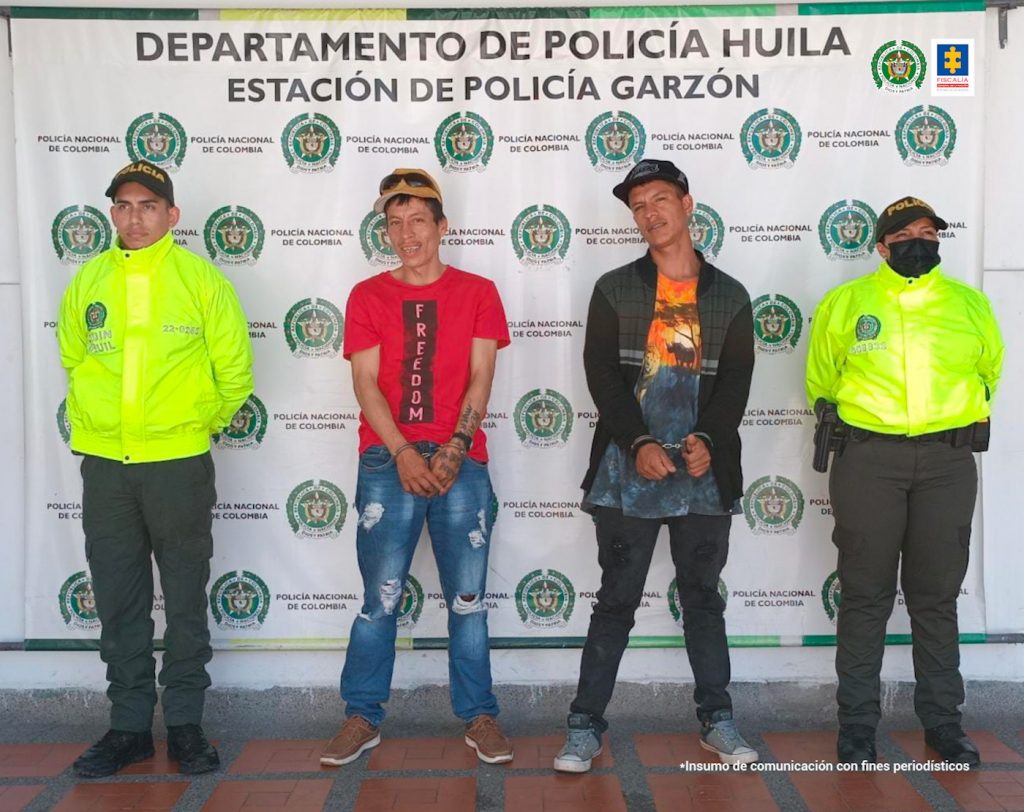 En la fotografía aparecen dos capturados junto a personal de Fiscalía General de La Nación y Policía Nacional. En la parte posterior de la imagen se ven banners de Policía Nacional y la Fiscalía General de la Nación.