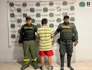 En la fotografía aparece un capturado, junto a personal de Fiscalía General de la Nación y Policía Nacional. En la parte posterior de la imagen se ven banners de Policía Nacional y la Fiscalía General de la Nación.