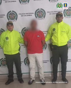 En la imagen se ve una persona de camiseta roja, detenida entre dos uniformados de la Policía.