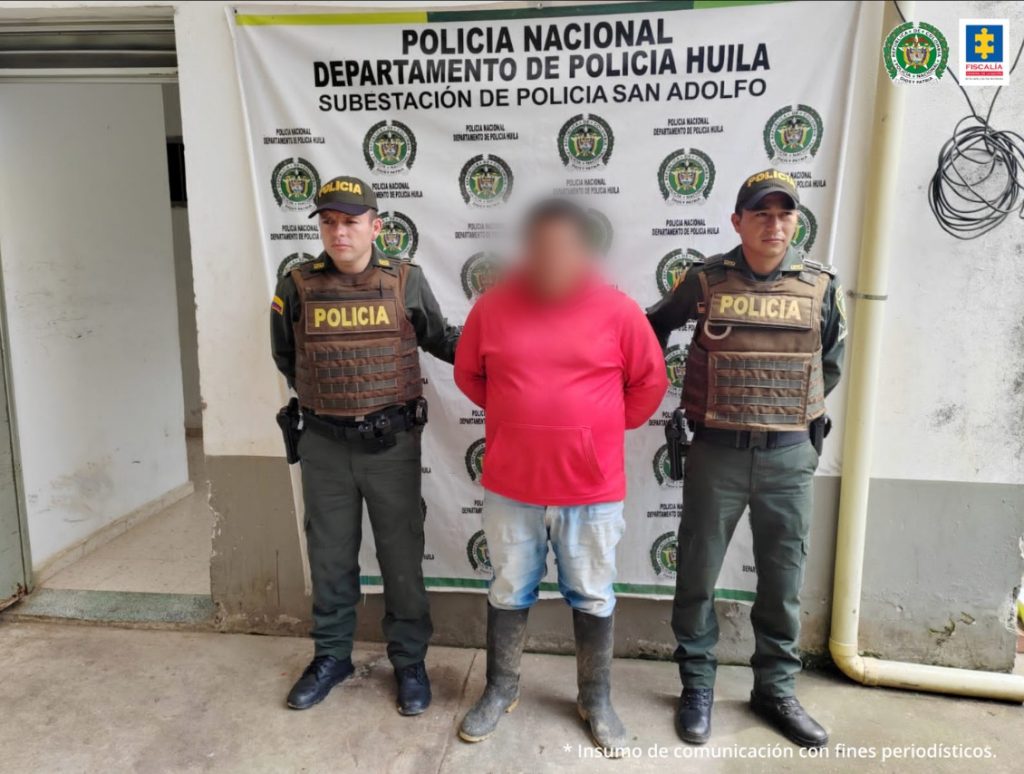 En la fotografía aparece un capturado junto a personal de Policía Nacional. En la parte posterior de la imagen se ven banners de Policía Nacional y la Fiscalía General de la Nación.