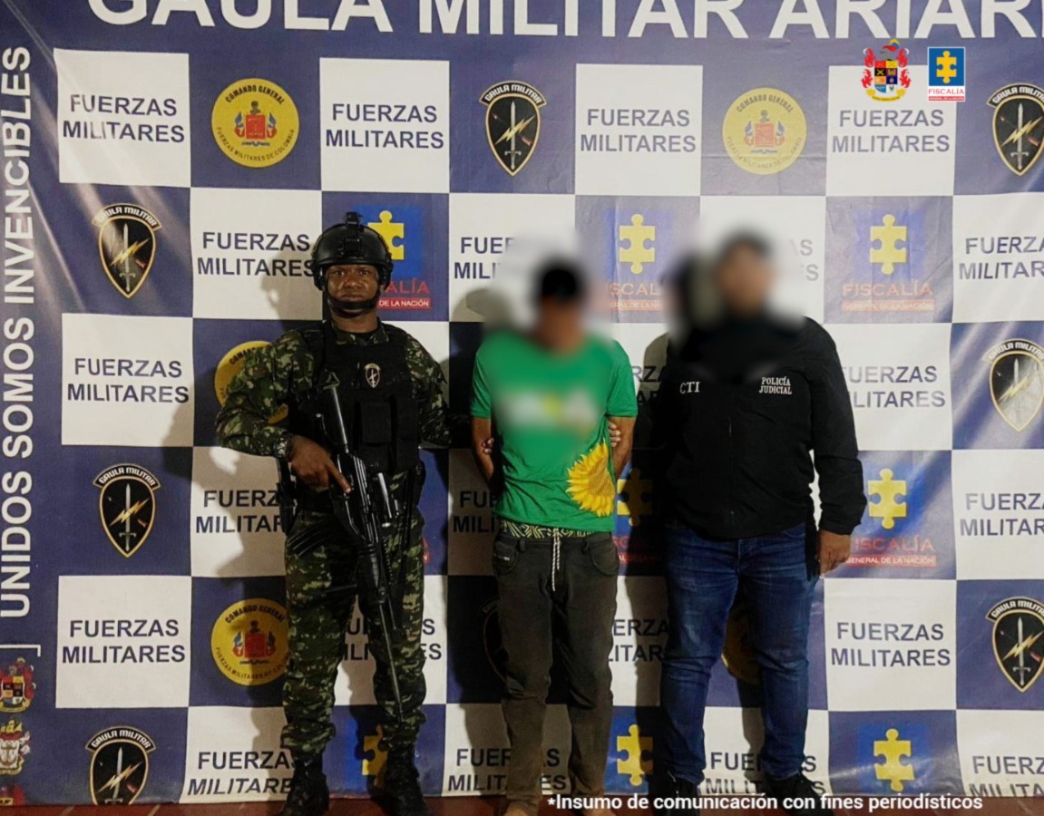 capturado de frente custodiado por investigador del CTI de la Fiscalía y un soldado. Detrás banner del grupo Gaula Militar.