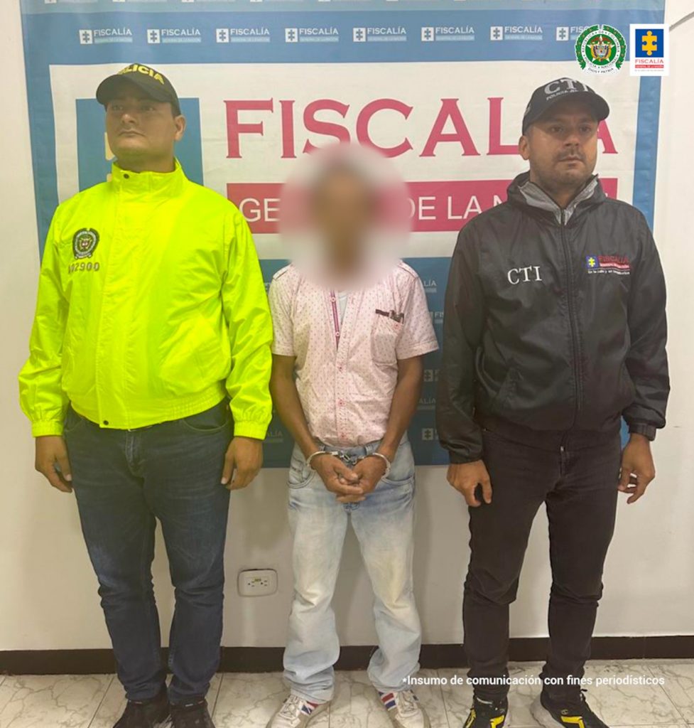 capturdao de frente esposado manos adelante custodiado por un investigador de la Fiscalía. Detrás banner de la Fiscalía.