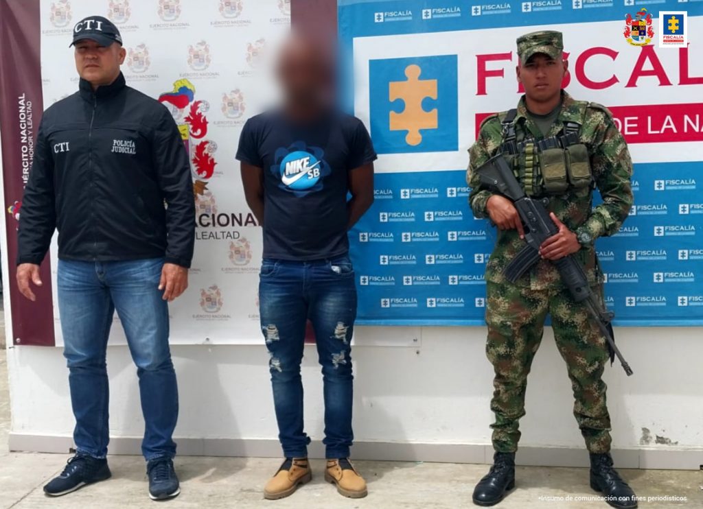 En la fotografía aparece un capturado junto a personal de Fiscalía General de La Nación y Ejército Nacional. En la parte posterior de la imagen se ven banners de Ejército Nacional y la Fiscalía General de la Nación.