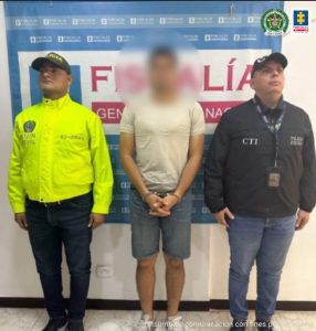 capturado esposado de frente custodiado por investigador del CTI de la Fiscalía y policía. Detrás banner de la Fiscalía.
