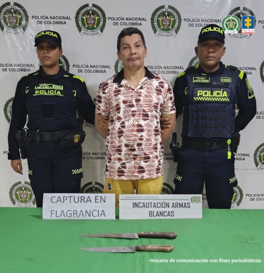 En la imagen aparece un hombre con camisa de flores y bermuda amarilla entre dos uniformados de la Policía. Frente a él en una mesa, dos armas cortopunzantes.