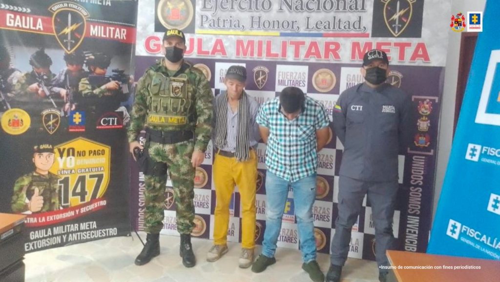 En la imagen están los capturados esposados con los manos atrás custodiados por un investigador del CTI de la Fiscalía y un militar y detrás banner de Fiscalía y Ejército.