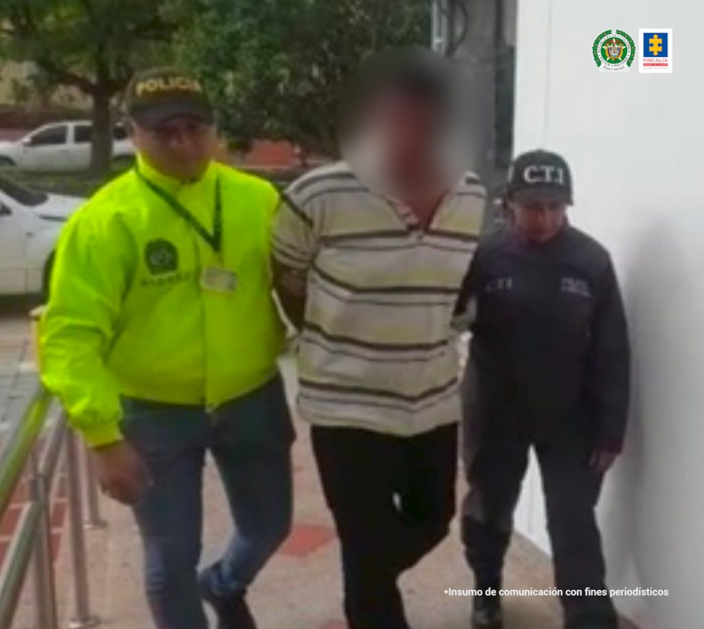 En la imagen se ve una persona caminando detenida entre un uniformado de la Policía y otro de la Fiscalía. 