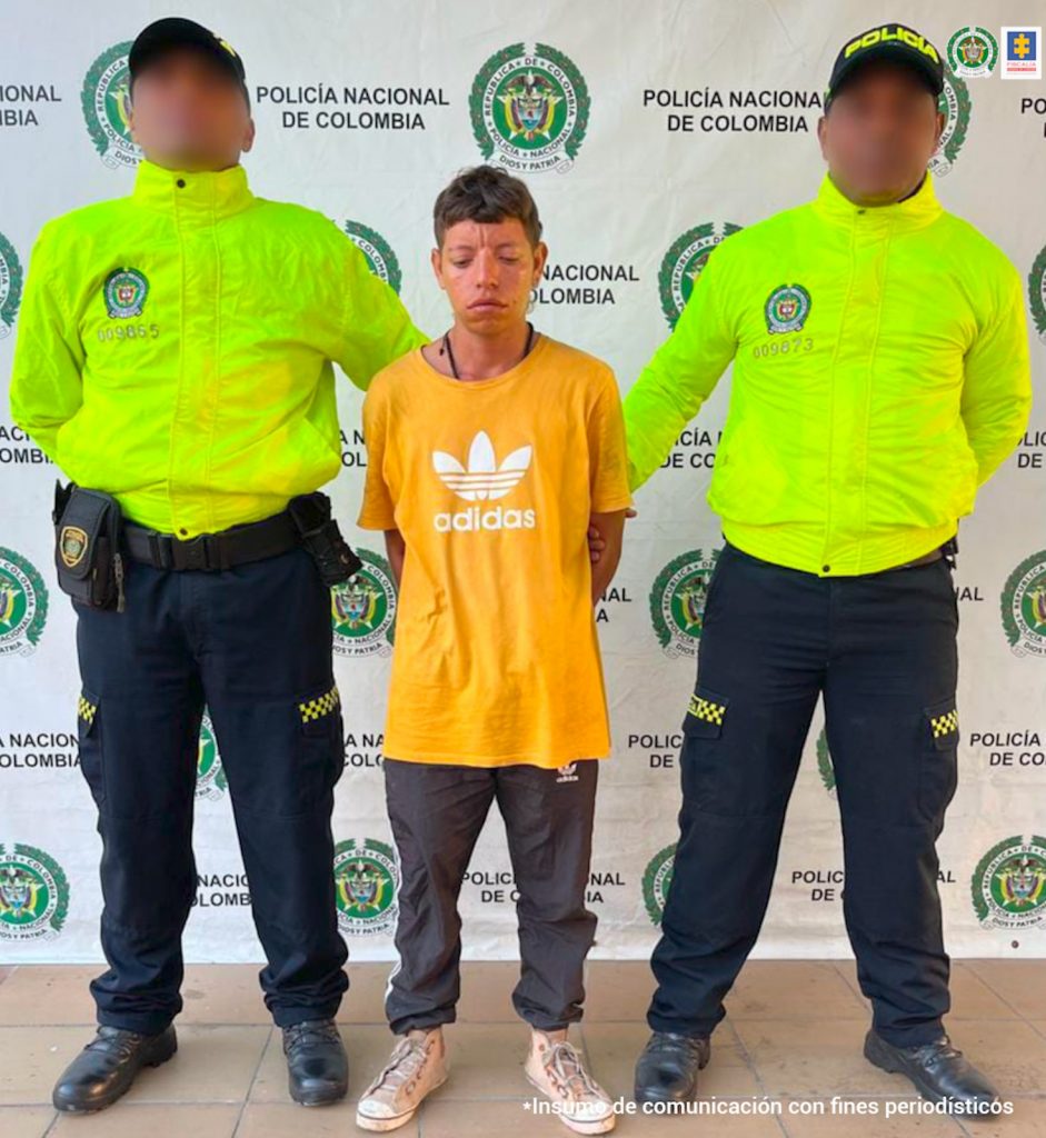 En la imagen aparece una persona de suéter amarillo, entre dos uniformados de la Policía. 