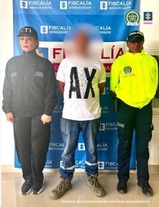 En la fotografía aparece el hoy imputado, de pie y con los brazos atrás. Viste camiseta blanca con las letras AX grandes estampadas en color negro; jean azul desgastado y zapatos color caqui. Al lado derecho de él hay una servidora del CTI de la Fiscalía y al lado izquierdo un uniformado de la Policía Nacional. Detrás de ellos hay un pendón institucional de la Fiscalía.