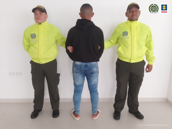 En la imagen se ve un hombre de espaldas, con un buso negro, detenido entre dos policías.