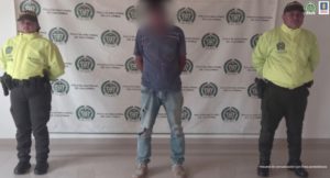 En la imagen se ve una persona capturada, frente a una mesa y entre funcionarios de la Policía.