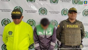 En la imagen se ve una persona de buso verde, entre dos uniformados de la Policía.