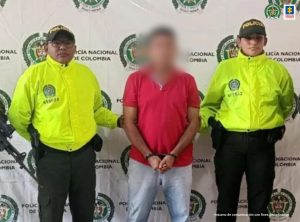 En la fotografía aparece un hombre capturado, acompañado de dos uniformados de La Policía Nacional. En la parte posterior un banner con logos de la entidad.