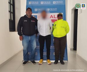 En la imagen se ve una persona de suéter blanco, entre uniformados del CTI y de la Policía Nacional.