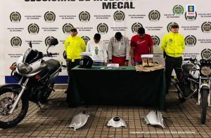 En la fotografía se aprecia a los tres presuntos integrantes del grupo. Uno de ellos viste camiseta roja de manga corta. Otro viste buzo blanco con estampados de rombos negros y pantalón rojo. Un tercero viste buzo blanco con un estampado en jean azul. A lado y lado de ellos hay uniformados de la Policía Nacional. Delante de ellos hay una mesa con mantel verde y sobre ella hay un casto de motociclista, cuatro celulares y un chaleco multipropósito con botas de color miel. En el piso hay partes de motocicletas y a lado y lado se ven dos motocicletas. Detrás de ellos hay un pendón institucional de la Policía.