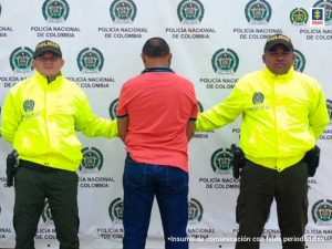 En la fotografía aparece un capturado de espalda, junto a dos uniformados de la Policía Nacional. En la parte posterior de la imagen un banner de la entidad.