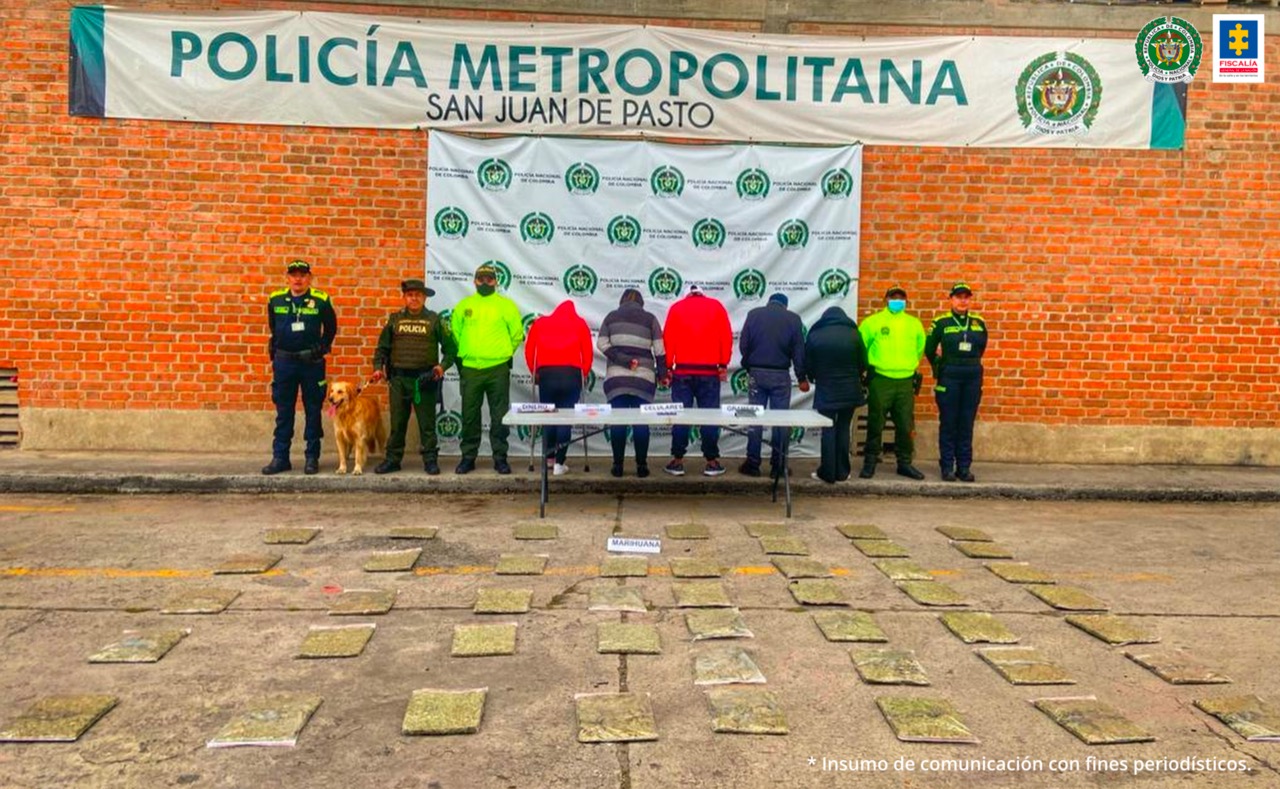En la fotografía aparecen cinco personas capturadas, entre ellas dos mujeres, junto a cuatro agentes de la Policía Nacional. En la parte posterior de la imagen se ve una mesa con bolsas transparentes, un teléfono celular y una gramera electrónica. En el piso, extendidas, varias bolsas plásticas con marihuana.