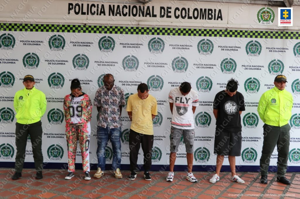 Se observan 5 personas capturadas yn fila y a cada extremos un funcionario de la Policía Nacional Atrás un baking de Policía Nacional