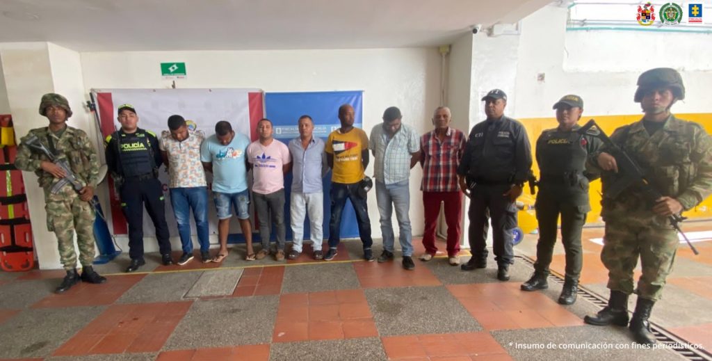 En la fotografía aparecen siete personas capturadas, acompañados de varios uniformados de la Policía y el Ejército Nacional. En la parte posterior un banner con el logo de la entidad y de la Fiscalía General de la Nación.