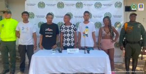En la fotografía aparecen cinco personas capturadas, acompañadas de dos uniformados de la Policía Nacional. En la parte posterior un banner con logos de la entidad.