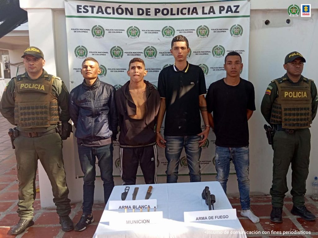 En la fotografía aparecen cuatro personas capturadas, acompañadas de dos uniformados de la Policía Nacional. En la parte posterior un banner con logos de la entidad.  