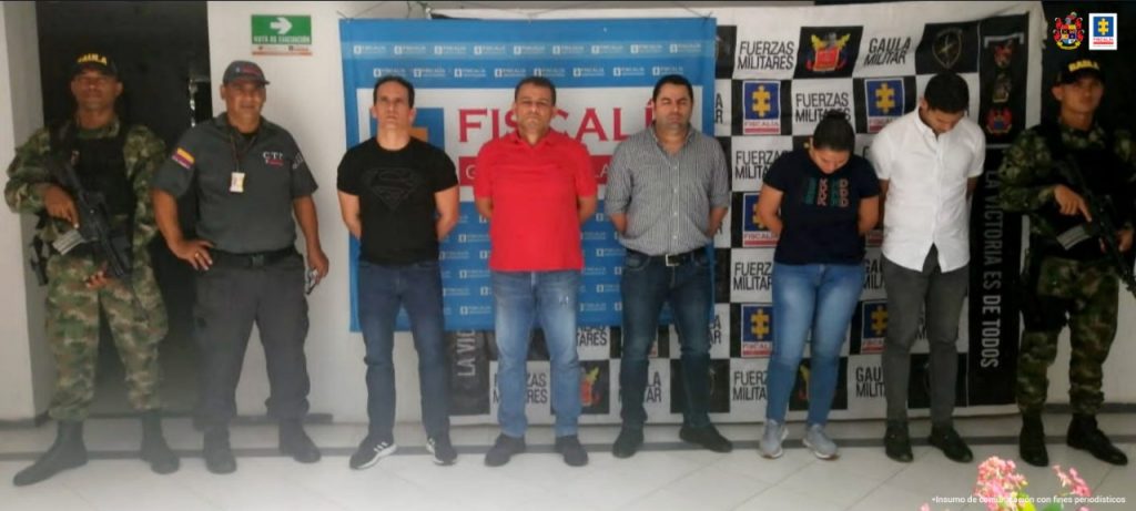 En la fotografía aparecen cinco personas capturadas, una mujer y cuatro hombres, junto a personal del CTI y el Ejército Nacional. En la parte posterior de la imagen se ven dos banners con los logos de la Fiscalía y el Ejército.