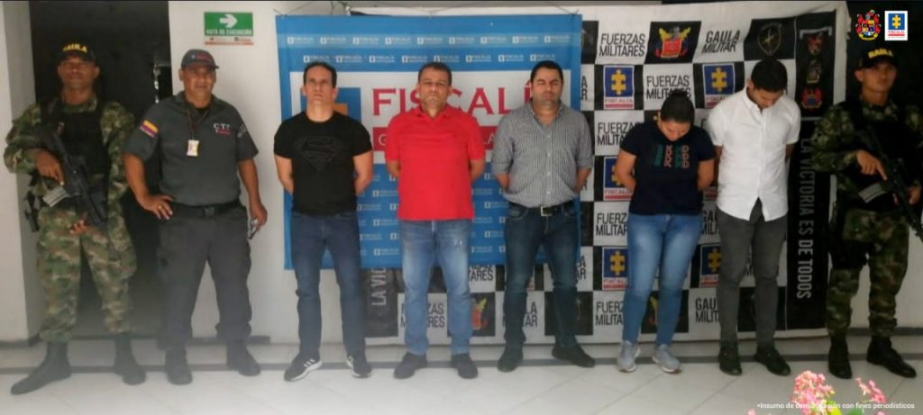 En la fotografía aparecen cinco personas capturadas, una mujer y cuatro hombres, junto a personal del CTI y el Ejército Nacional. En la parte posterior de la imagen se ven dos banners con los logos de la Fiscalía y el Ejército.    