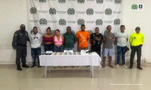 En la imagen se ven ocho personas frente a una mesa con material incautado y entre dos uniformados de la Policía y el CTI.  
