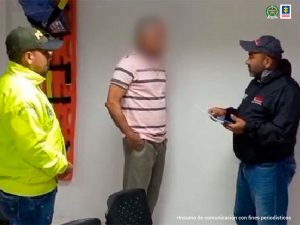 En la imagen se ve una persona detenida frente a un investigador que le lee sus derechos y junto con un policía.
