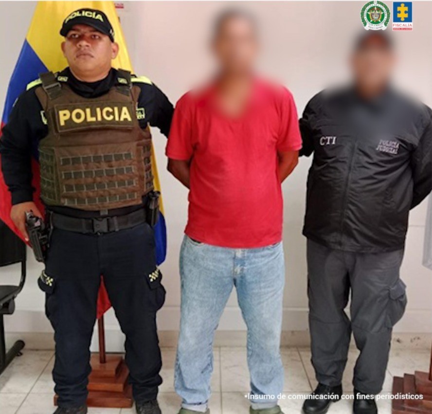 En la imagen aparece una persona de suéter rojo y jean entre dos uniformados del CTI y la Policía Nacional.