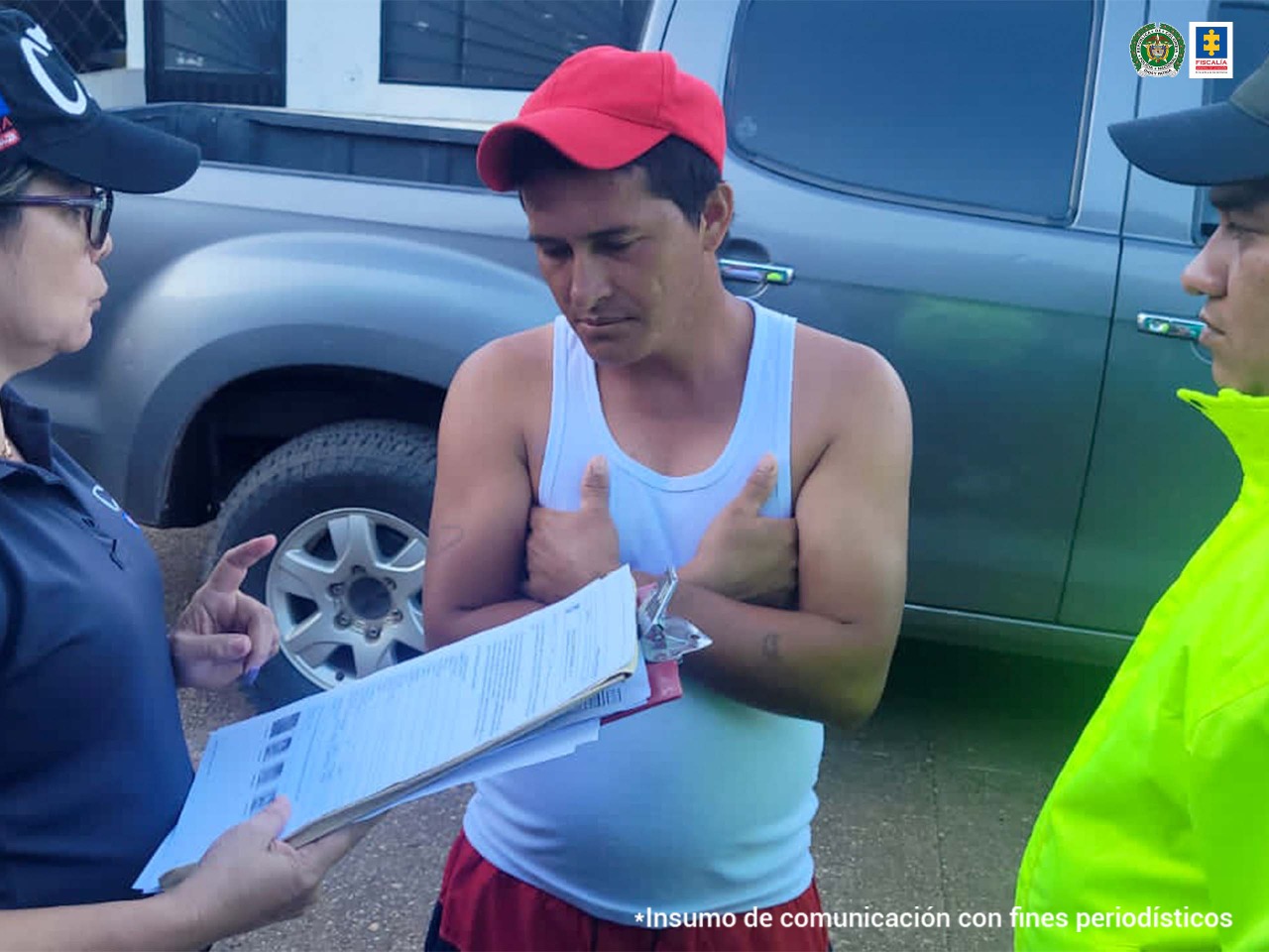 Hombre capturado con gorra roja y brazos cruzados. Acompaña una funcionaria del CTI de la Fiscalía que le lee los derechos del capturado y un uniformado de la Policía Nacional.