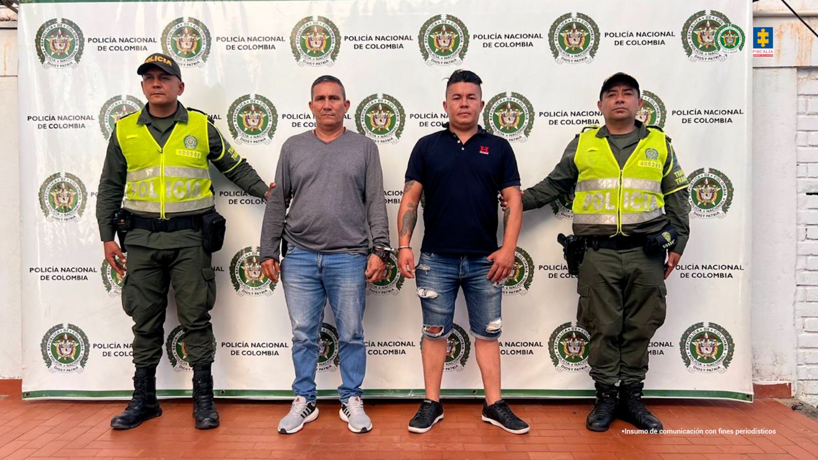 Los capturados se encuentran de frente y custodiados por dos uniformados de la Policía Nacional. En la foto se ve de fondo un backing de la Policía Nacional.