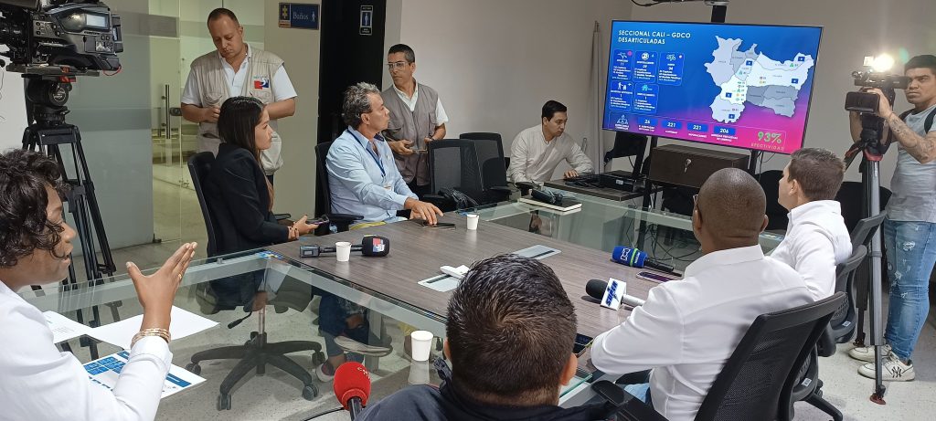 En la foto aparece la Directora Seccional de Fiscalías Cali, con periodistas de la región, alrededor de una mesa de vidrio, mirando todos hacia una pantalla donde se ve proyectado un mapa de las comunas de Cali.