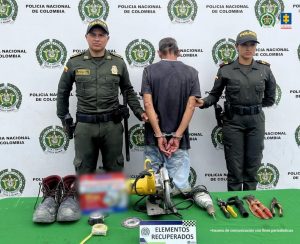 En la fotografía se aprecia de pie, de espaldas a la cámara, con los brazos atrás y esposado a Rafael Albeiro Osorio. Viste camiseta de manga corta gris y jean azul. A los extremos hay uniformados de la Policía Nacional. Enla parte delantera hay una superfice de color verde y hay sobre ella varios elementos utilizados en la construcción. En la parte posterior hay un pendón institucional de la Policía.
