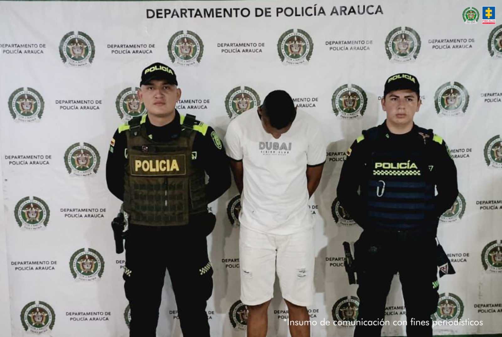 El hombre aparece en el centro de la imagen, con la cabeza agachada y las manos esposadas en la espalda. Lo rodean miembros de la Policía y al fondo hay un backing de la misma institución.