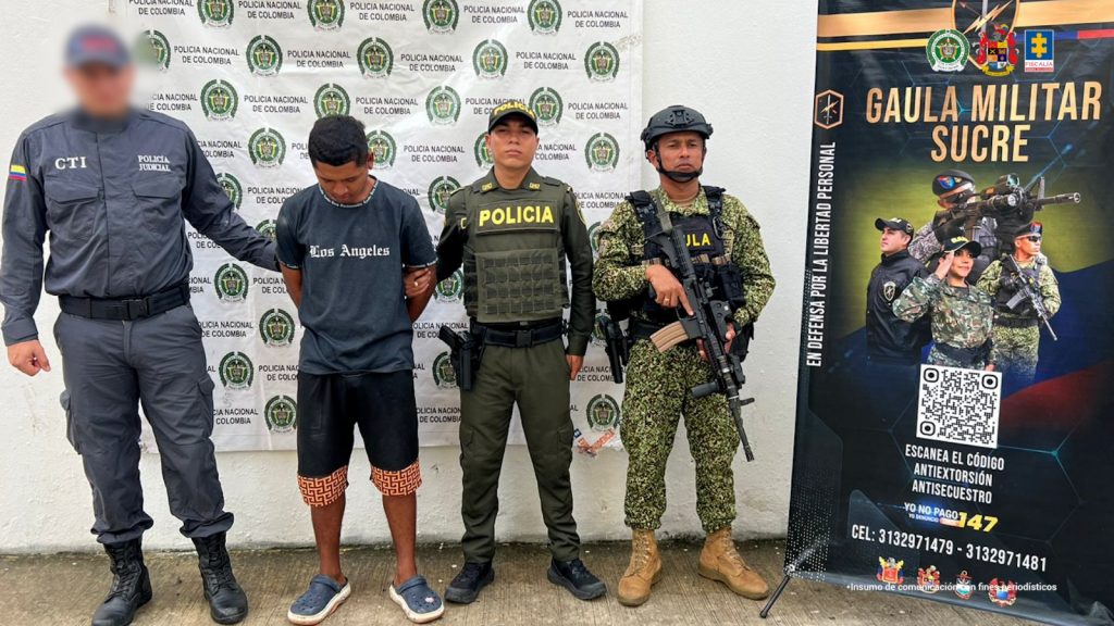 En la imagen sale una persona de suéter y bermuda negra detenida entre un uniformado de la Policía, la Armada y el CTI de la Fiscalía.