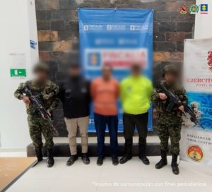Se visualiza al capturado con el rostro difuminado junto a un investigador del CTI y uniformados del Ejército y Policía Nacional. Detrás de ellos los banners que identifican a la Fiscalía General de la Nación y del Ejército Nacional.