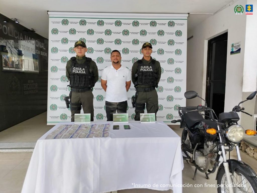 En la imagen aparece una persona de suéter blanco, entre dos uniformados del Gaula de la Policía Nacional.
