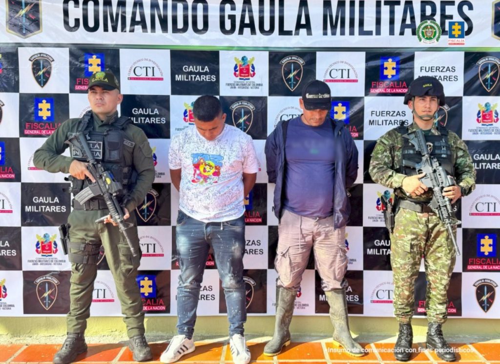 Los capturados se encuentran de frente y custodiados por uniformados del Gaula de la Policía Nacional. Detrás se observa un backing de la Policía Nacional.