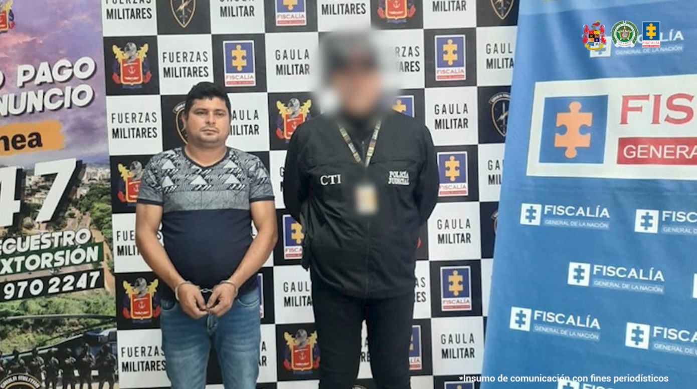 Se visualiza al capturado junto a un investigador del CTI. Detrás los banners que identifican al Gaula Militar y a la Fiscalía General de la Nación.