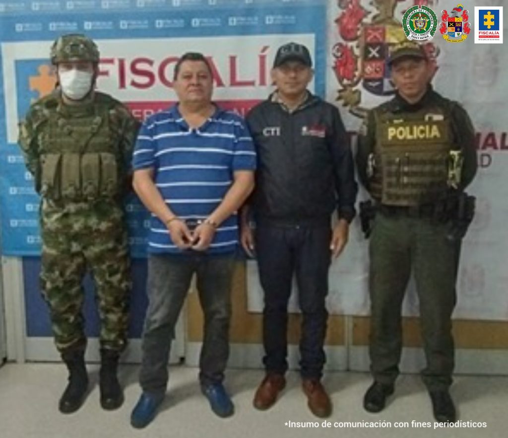 en la imagen se ve una persona detenida bajo custodia del CTI, Ejército y Policía. Detrás suyo backings institucionales de las dos primeras instituciones.