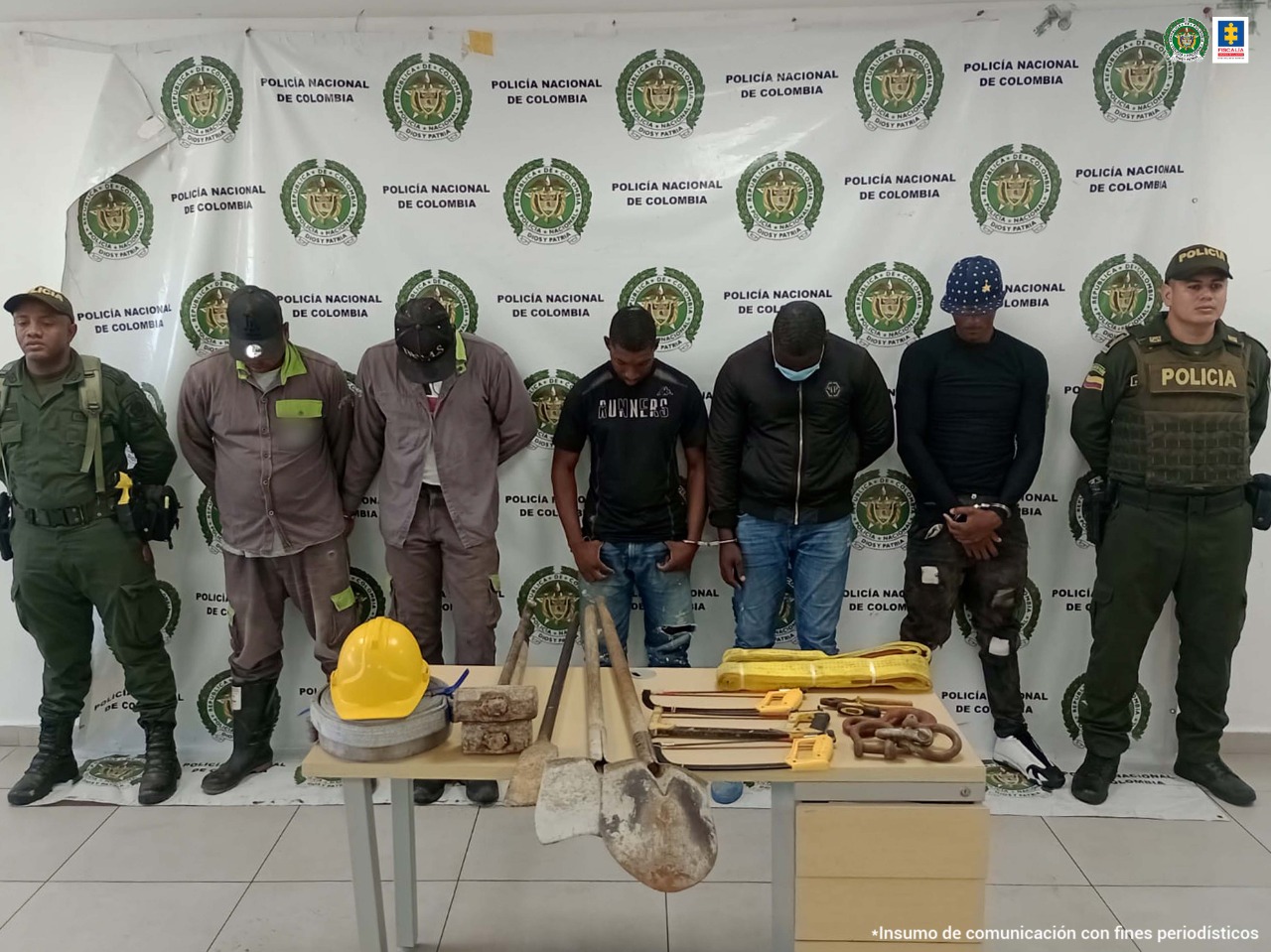 En la fotografía se observan a los cinco capturados junto a dos agentes de la Policía Nacional. En la parte superior se observa una mesa con palas, una barra de hierro, un casco, alicates, 2 porras, un destornillar, dos ligas, entre otros elementos incautados