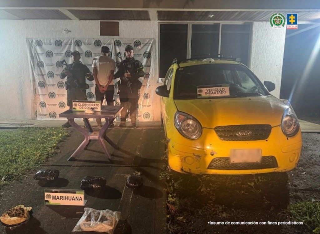 La fotografía fue tomada en la noche. Aparece de espaldas a la cámara, con los brazos atrás y esposado Roger Alejandro Sepúlveda Buriticá. Viste con camisa, de mangas cortas y color blanco; pantalón oscuro. En sus extremos hay uniformados de la Policía Nacional. Delante de ellos hay una mesa y sobre ella hay una bolsa plástica transparente con contenido blanco. Asimismo, hay un letrero que dice: ‘Clorhidrato de cocaína’. Sobre el piso hay varios paquetes envueltos en plástico de color negro y transparente. Y sobre ella hay un letrero que dice: ‘Marihuana’. En el extremo derecho de la toma hay un vehículo tipo taxi. En la parte posterior, hay un pendón institucional de la Policía.