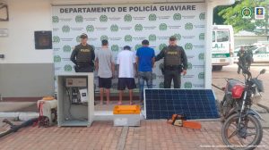 están los capturados de espaldas custodiados por dos policías, delante los elementos incautados. Detrás banner de la Policía Nacional.